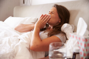 Frau mit Erkältung im Bett: Medikamente helfen beim Behandeln und Vorbeugen.