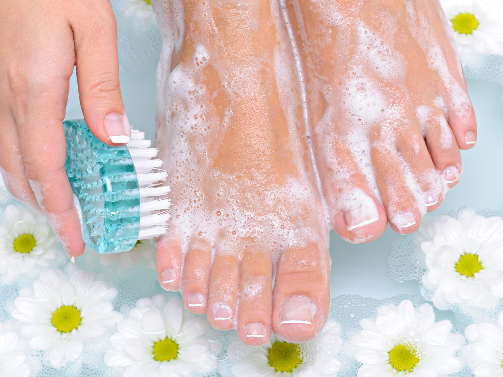 Foto von Füßen in einem Fußbad mit Blüten, Seifenschaum und Bürste